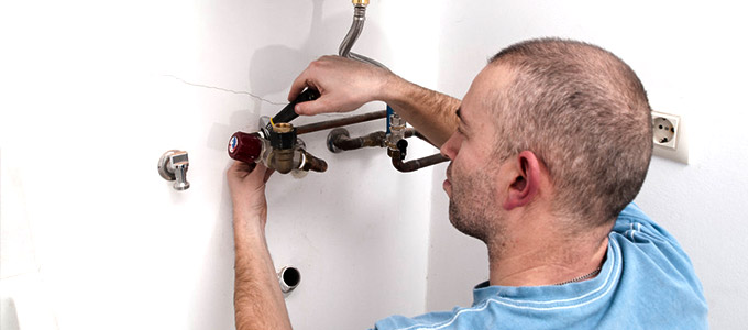 a plumber working on pipes while installing a modern hot water heater inside of a toronto home